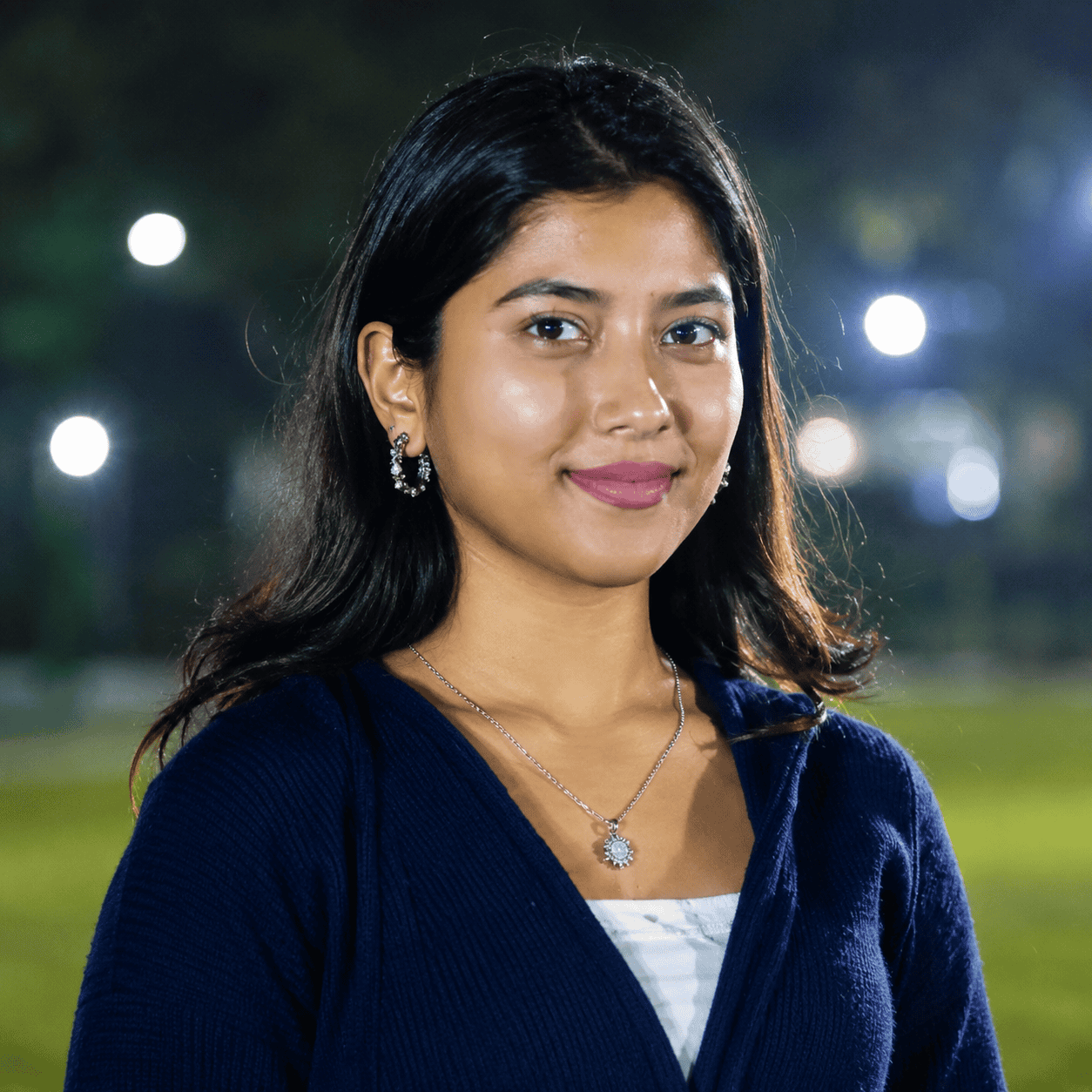 Young woman smiling outdoors at night, showcasing confidence and style.